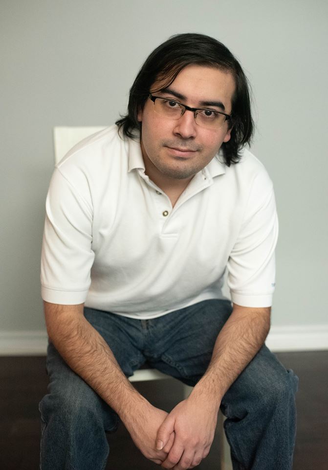 Carlos Alonzo Morales wearing white polo shirt and blue jeans sitting in a chair