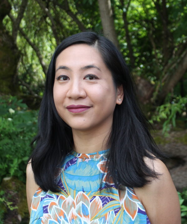headshot of Tessa Barbosa, a Filipina-Canadian woman with straight black hair wearing a blue floral top standing in front of greenery